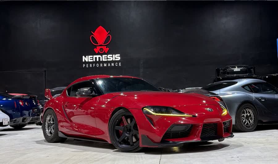 Cars parked in front of the illuminated Nemesis Performance logo wall